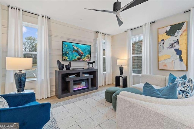 living area featuring a healthy amount of sunlight, ceiling fan, tile patterned flooring, and a glass covered fireplace