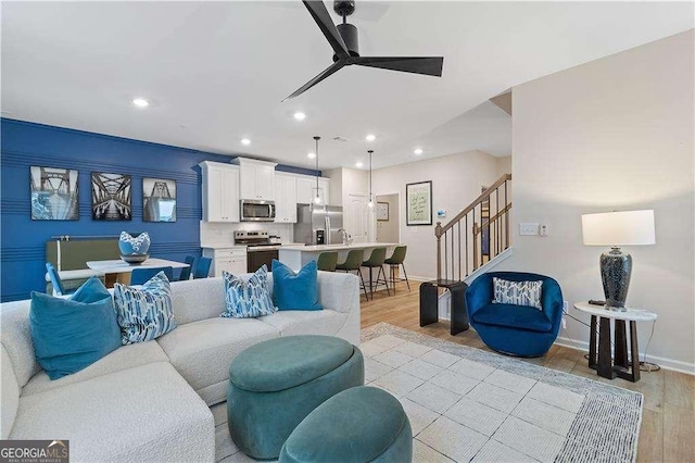 living area with recessed lighting, a ceiling fan, baseboards, stairway, and light wood finished floors