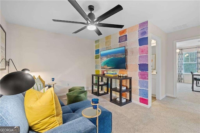 carpeted living area featuring ceiling fan, an accent wall, visible vents, and baseboards