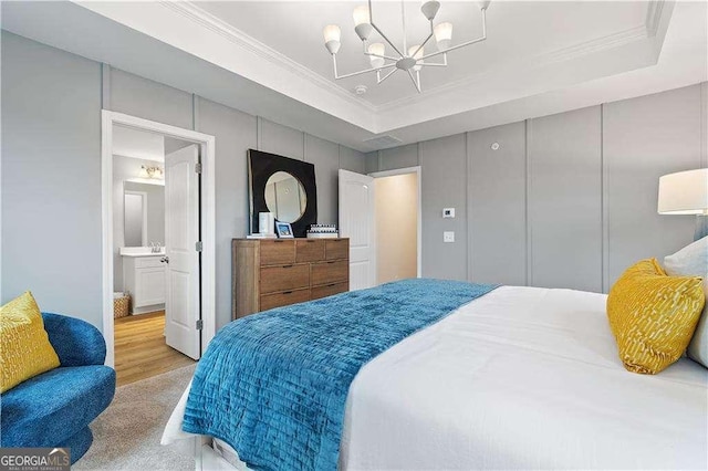 bedroom with ornamental molding, ensuite bath, a raised ceiling, and a notable chandelier