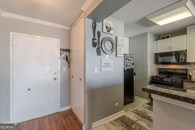 kitchen featuring white cabinetry, tasteful backsplash, dark stone counters, ornamental molding, and black appliances