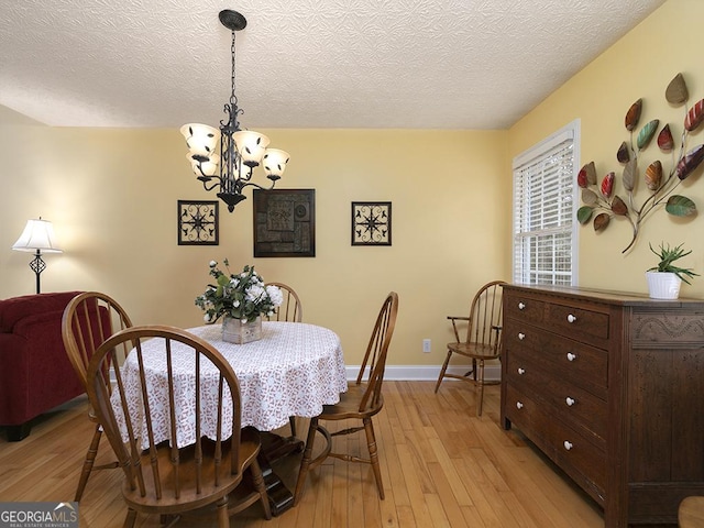 dining room with light wood-type flooring, a textured ceiling, and a notable chandelier