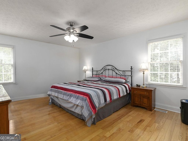 bedroom with ceiling fan, light wood-type flooring, multiple windows, and a textured ceiling