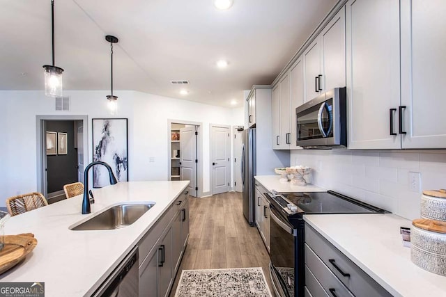 kitchen featuring appliances with stainless steel finishes, tasteful backsplash, sink, hanging light fixtures, and gray cabinetry