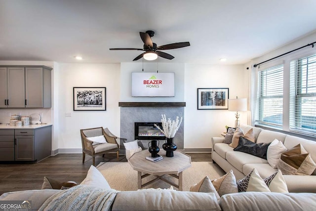 living room with ceiling fan, a tiled fireplace, and dark hardwood / wood-style floors