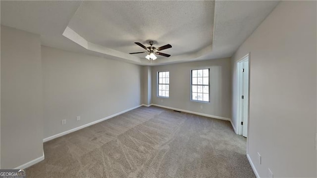 spare room featuring ceiling fan, a textured ceiling, a tray ceiling, and light carpet