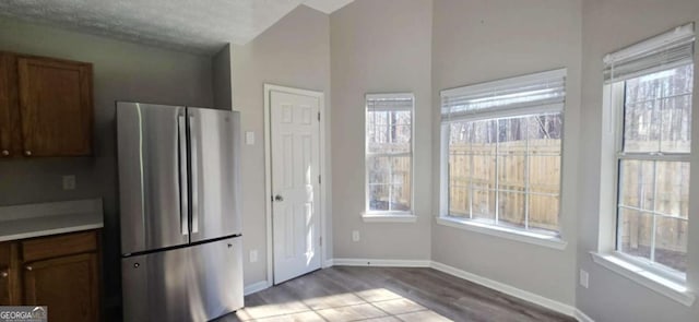 kitchen with vaulted ceiling, stainless steel refrigerator, a textured ceiling, and light hardwood / wood-style flooring