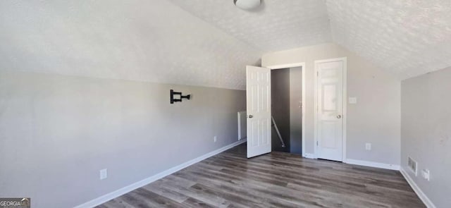 additional living space with vaulted ceiling, dark wood-type flooring, and a textured ceiling