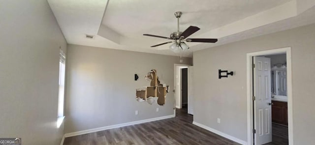 unfurnished bedroom featuring ensuite bathroom, ceiling fan, dark hardwood / wood-style flooring, and a raised ceiling