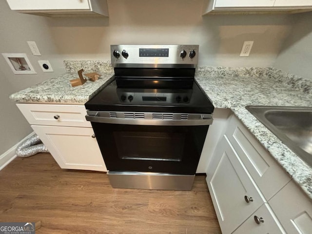 kitchen featuring stainless steel electric stove, light hardwood / wood-style floors, light stone counters, and white cabinets