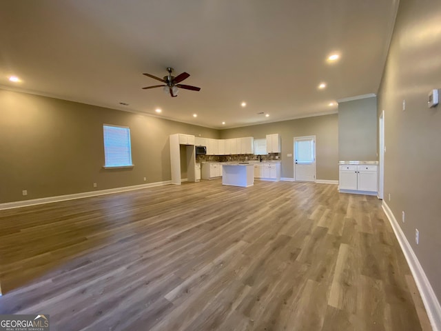 unfurnished living room featuring ceiling fan, light wood-type flooring, and crown molding