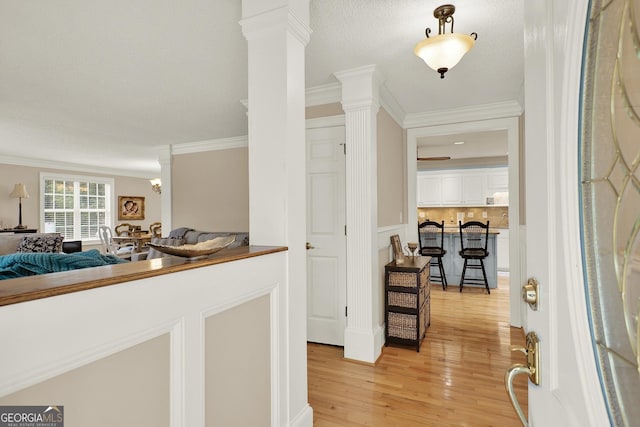 entrance foyer with crown molding, light hardwood / wood-style floors, and decorative columns