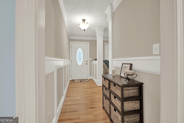 entryway with crown molding, light wood-type flooring, a textured ceiling, and ornate columns