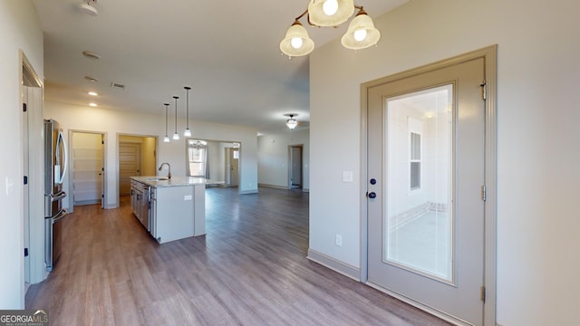 kitchen with light hardwood / wood-style floors, pendant lighting, sink, white cabinetry, and a kitchen island with sink