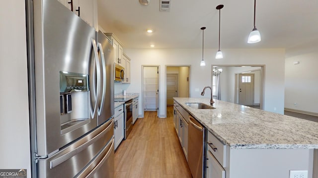 kitchen featuring appliances with stainless steel finishes, decorative light fixtures, a kitchen island with sink, white cabinets, and sink