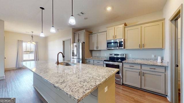 kitchen with stainless steel appliances, hanging light fixtures, and an island with sink