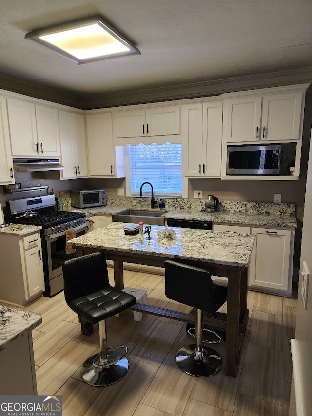 kitchen with light stone countertops, white cabinetry, stainless steel appliances, sink, and light wood-type flooring