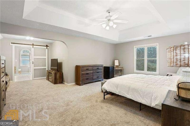 bedroom with ceiling fan, a tray ceiling, light carpet, and a barn door