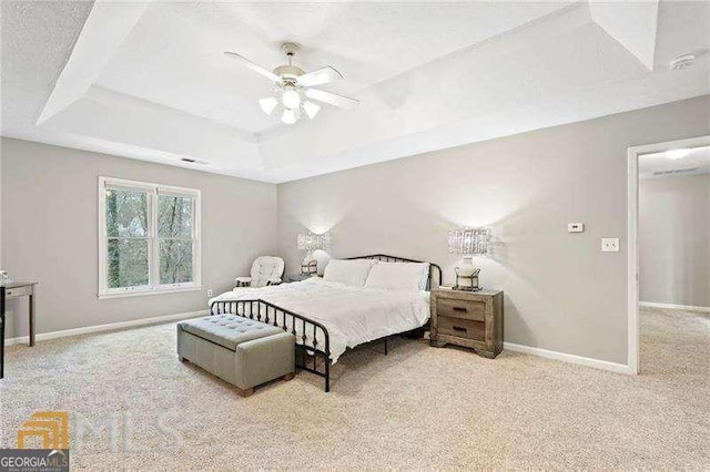 bedroom with ceiling fan, light colored carpet, and a tray ceiling