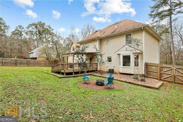 back of property with a wooden deck, an outdoor fire pit, and a lawn