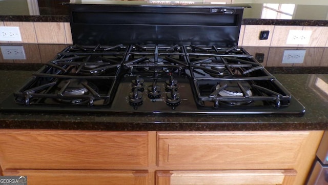 room details featuring black gas stovetop, backsplash, and dark stone countertops