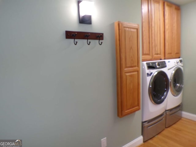 laundry area featuring washing machine and dryer, cabinets, and light hardwood / wood-style floors