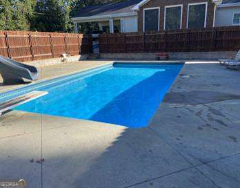 view of pool with a patio area, a water slide, and a diving board