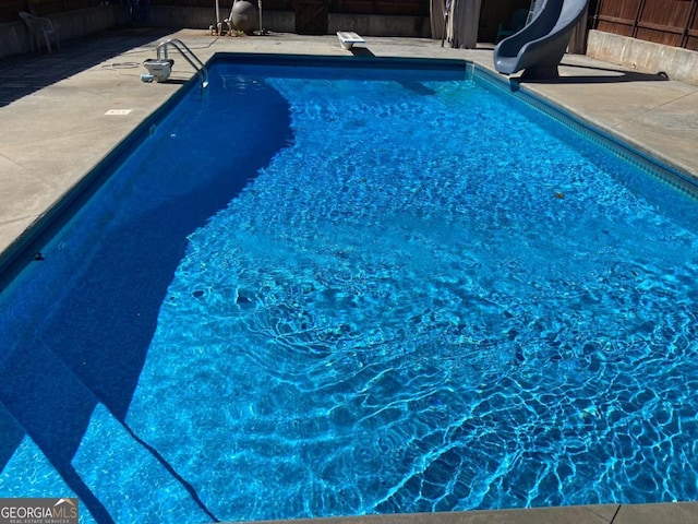 view of swimming pool featuring a diving board, a water slide, and a patio