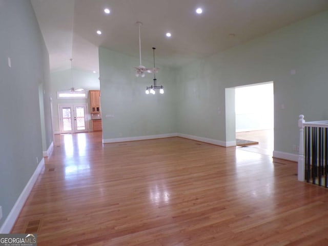 empty room with french doors, an inviting chandelier, a high ceiling, and light hardwood / wood-style flooring