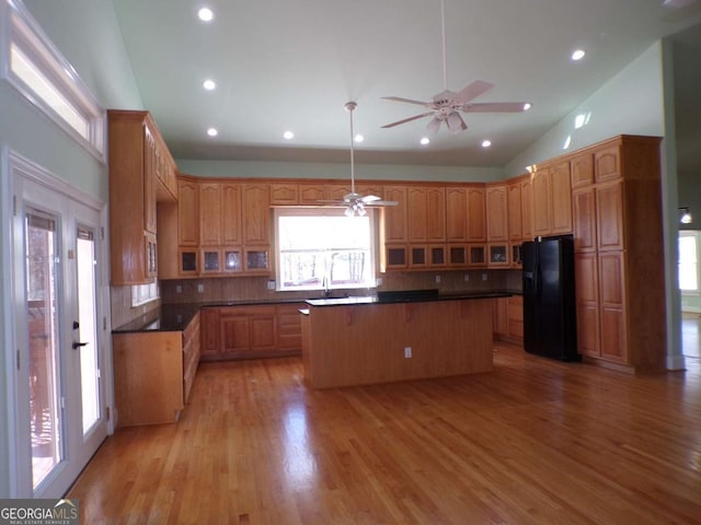 kitchen with a center island, backsplash, black fridge, light wood-type flooring, and ceiling fan