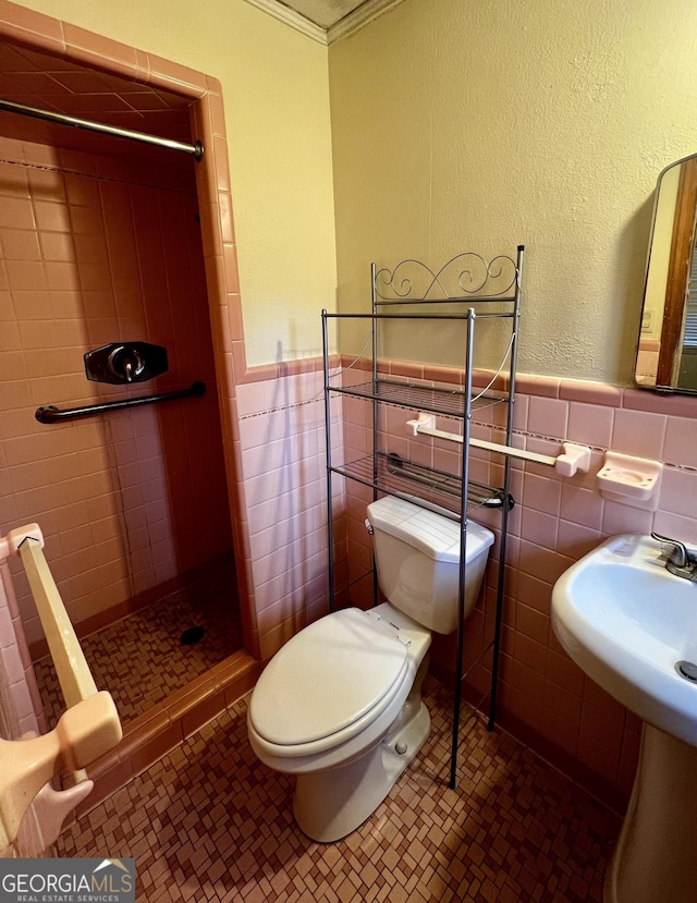 bathroom with toilet, tiled shower, tile walls, tile patterned floors, and ornamental molding