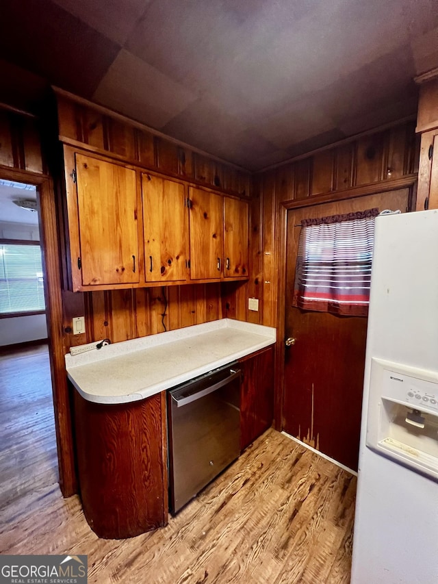 kitchen featuring dishwasher, white refrigerator with ice dispenser, wooden walls, and light hardwood / wood-style flooring