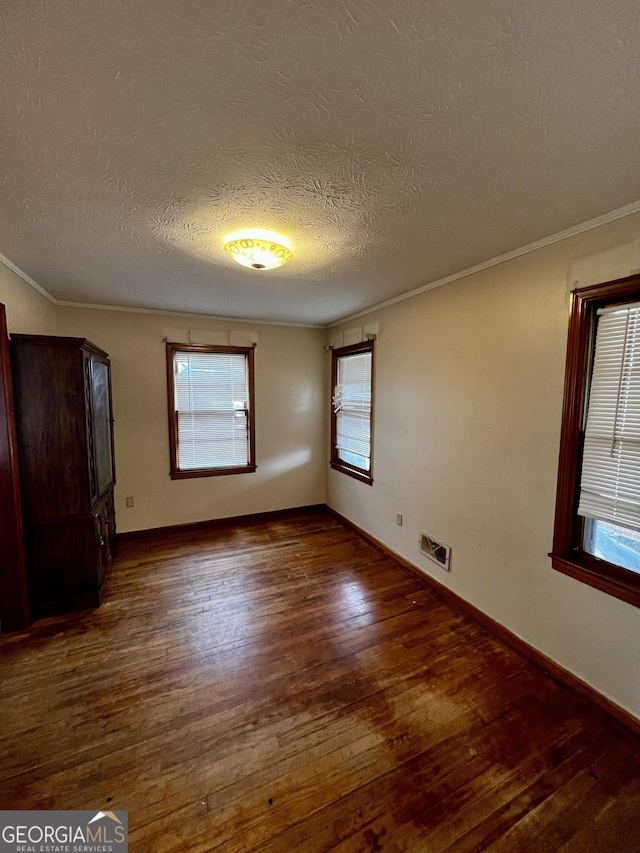 empty room with dark hardwood / wood-style flooring, ornamental molding, and a textured ceiling