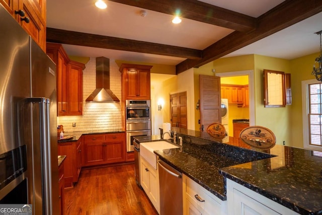 kitchen with tasteful backsplash, appliances with stainless steel finishes, wall chimney range hood, and dark stone counters