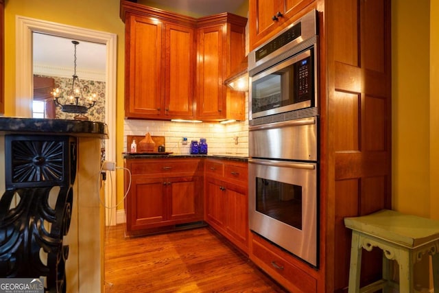 kitchen with dark stone countertops, an inviting chandelier, tasteful backsplash, hanging light fixtures, and light hardwood / wood-style flooring