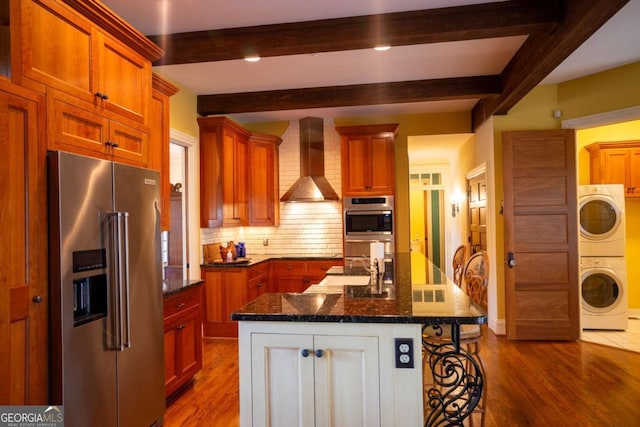 kitchen featuring stainless steel appliances, wall chimney exhaust hood, beam ceiling, and a center island with sink