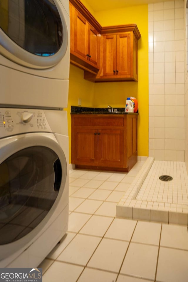 washroom featuring cabinets, light tile patterned floors, stacked washer / dryer, and sink