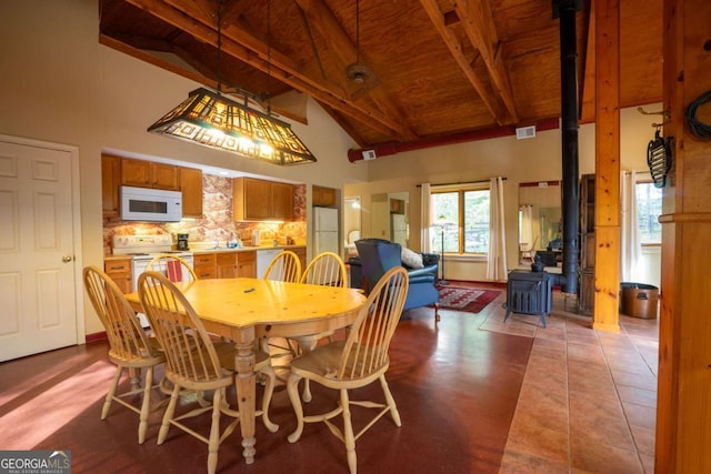 tiled dining room with a wealth of natural light, beam ceiling, a wood stove, and high vaulted ceiling