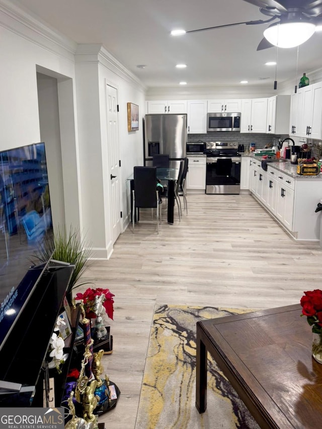 kitchen with backsplash, light hardwood / wood-style flooring, light stone countertops, appliances with stainless steel finishes, and white cabinets