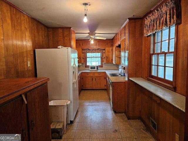 kitchen featuring sink, white fridge with ice dispenser, crown molding, and wood walls