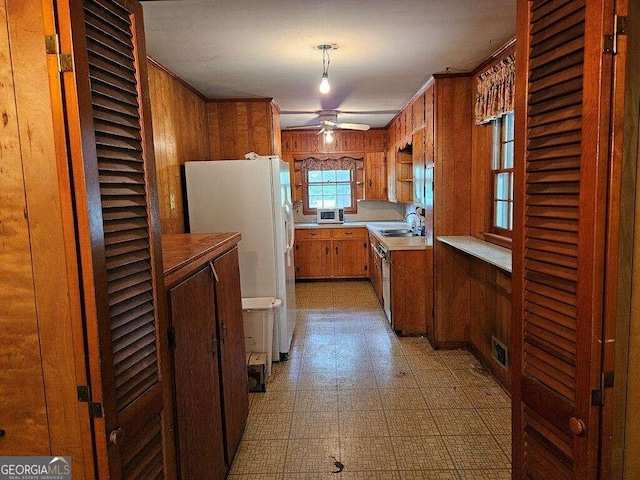 kitchen featuring white fridge with ice dispenser, pendant lighting, sink, wood walls, and ceiling fan