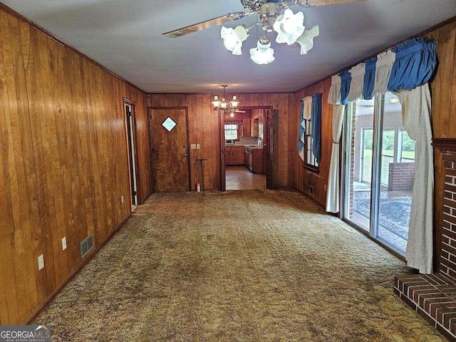 interior space featuring dark carpet, ornamental molding, wood walls, and a chandelier