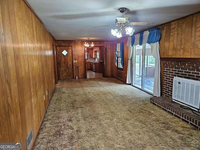 unfurnished living room featuring carpet floors, a fireplace, ceiling fan with notable chandelier, and wooden walls