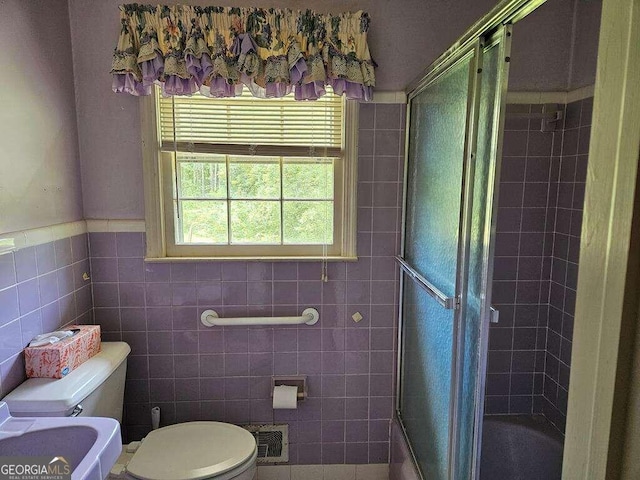 bathroom featuring toilet, bath / shower combo with glass door, and tile walls