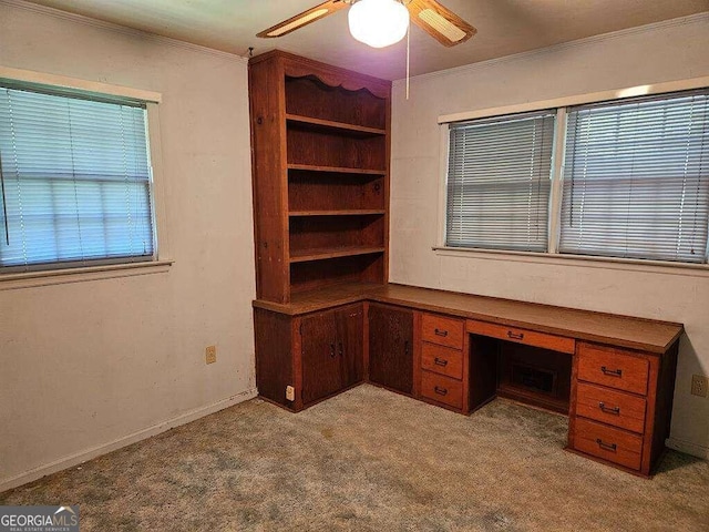 unfurnished office featuring ceiling fan, built in desk, plenty of natural light, ornamental molding, and light carpet