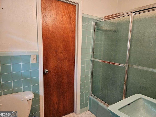 bathroom with bath / shower combo with glass door, tile walls, and toilet