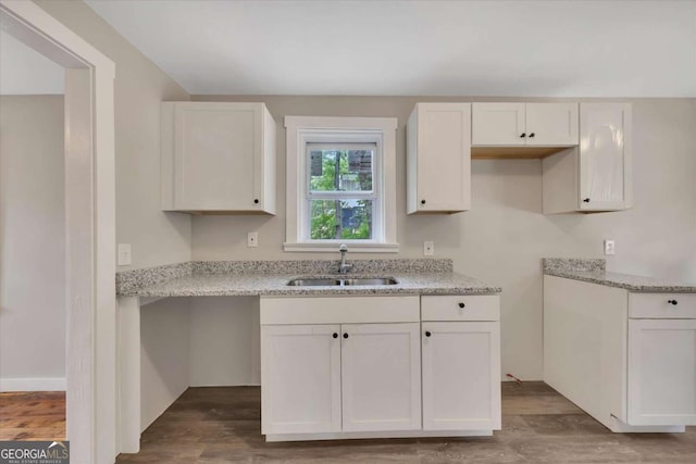 kitchen featuring wood-type flooring, sink, white cabinetry, and light stone counters