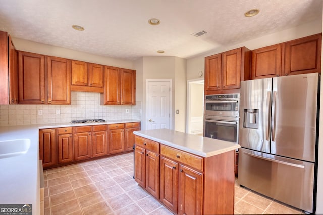 kitchen featuring a textured ceiling, appliances with stainless steel finishes, tasteful backsplash, and a kitchen island