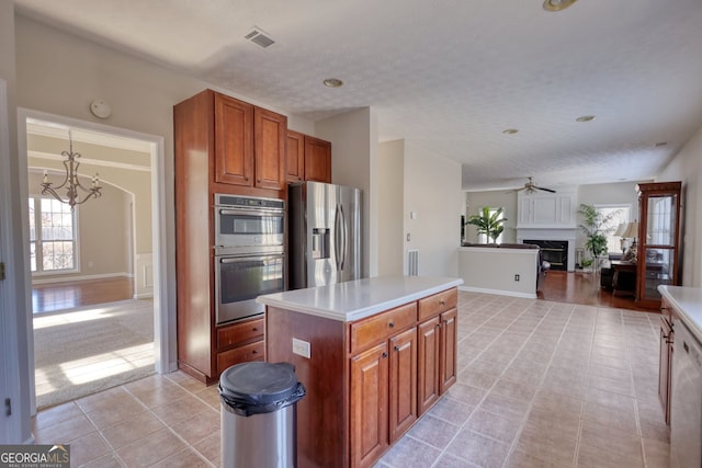 kitchen featuring a kitchen island, light tile patterned flooring, appliances with stainless steel finishes, a textured ceiling, and ceiling fan with notable chandelier