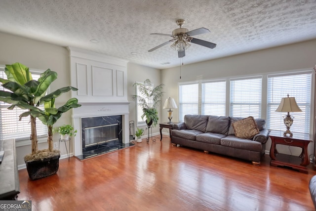 living room with ceiling fan, a fireplace, plenty of natural light, and a textured ceiling